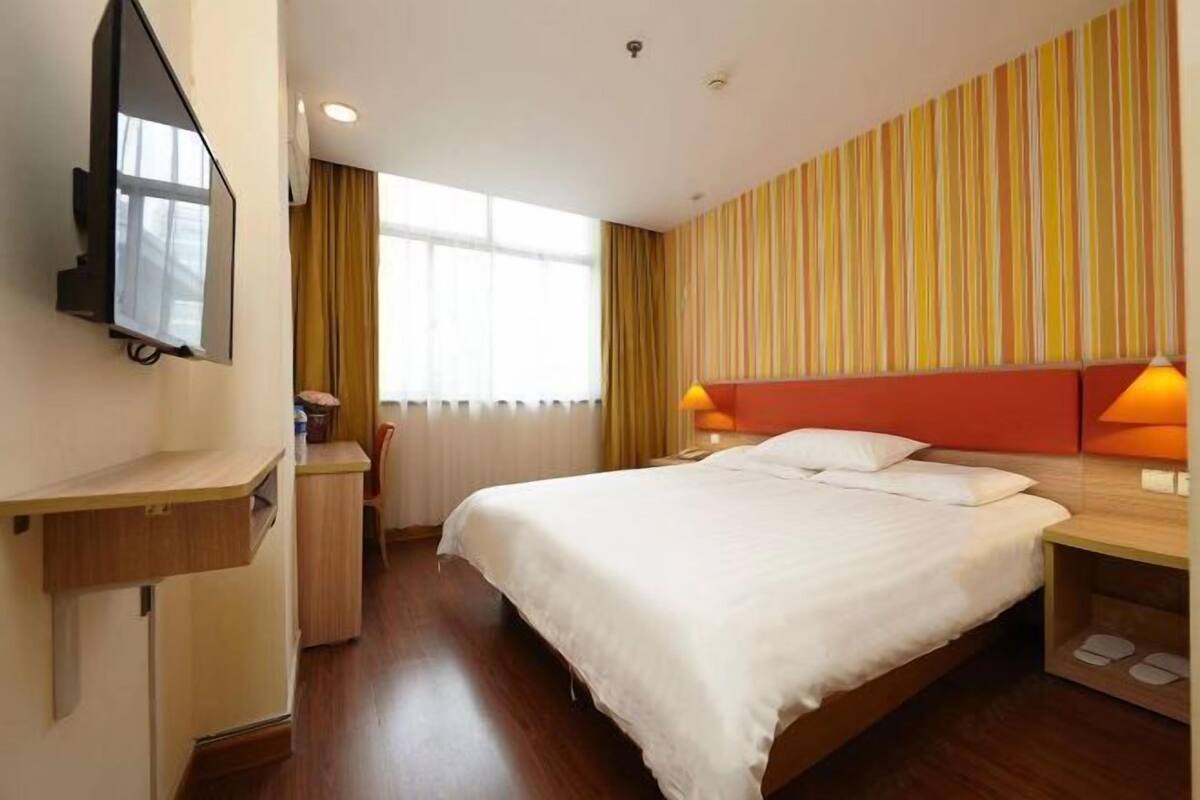 A hotel room with a bed, bedside tables, a desk, a TV, and a window with curtains.