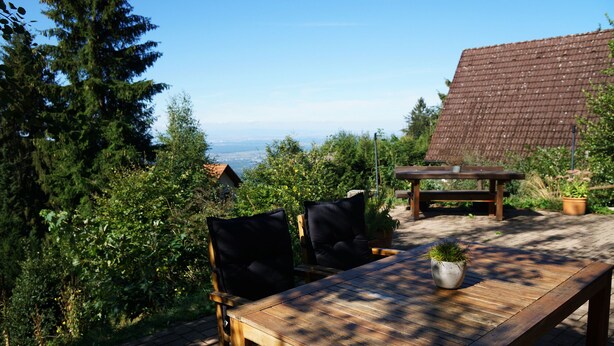 Un área de comedor al aire libre con mesa y sillas de madera, rodeada de vegetación y vistas al paisaje.