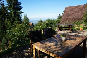 Un espace de restauration en plein air avec une table et des chaises en bois, entouré de verdure et offrant une vue sur le paysage.