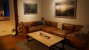 Un salón con un sofá de cuero marrón, una mesa de centro de madera y dos cuadros enmarcados en la pared.