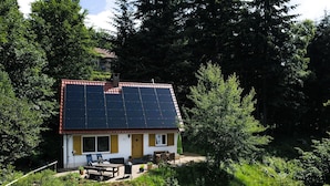 Una casa con tejado de paneles solares, rodeada de abundante follaje y árboles.