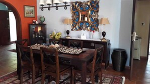 Un coin repas avec une table et des chaises en bois, un lustre, des miroirs décoratifs et un petit meuble surmonté d’un globe terrestre.