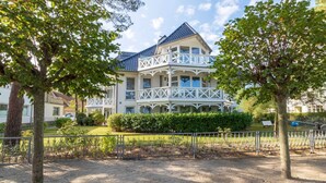 Ein großes, mehrgeschossiges Gebäude mit Balkon und einem Garten davor.