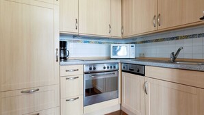 Eine Küche mit hellen Holzschränken, einem Edelstahlbackofen, einer Mikrowelle und einem Geschirrspüler.