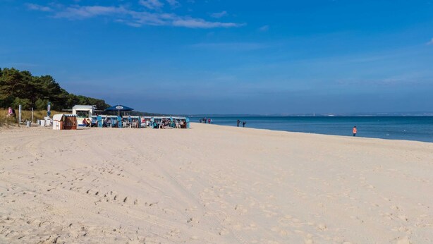 Ein Strand mit einer Reihe von Strandbuden und einigen Spaziergängern.