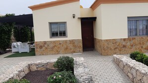 A two-story house with a stone facade, a covered patio with outdoor furniture, and a small garden area. - Romantic Villa Romeo with private pool, with stunning panoramic views of the (Costa Calma)
