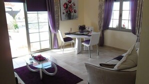 A dining area with a round glass table, white chairs, and a purple rug. There is a sofa and a window with curtains. - Romantic Villa Romeo with private pool, with stunning panoramic views of the (Costa Calma)