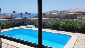 A swimming pool with a stone wall and plants, a view of the sea, and buildings in the background. - Romantic Villa Romeo with private pool, with stunning panoramic views of the (Costa Calma)