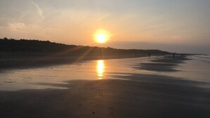 Una playa al atardecer, con el sol bajo en el horizonte, proyectando un brillo cálido sobre la arena.