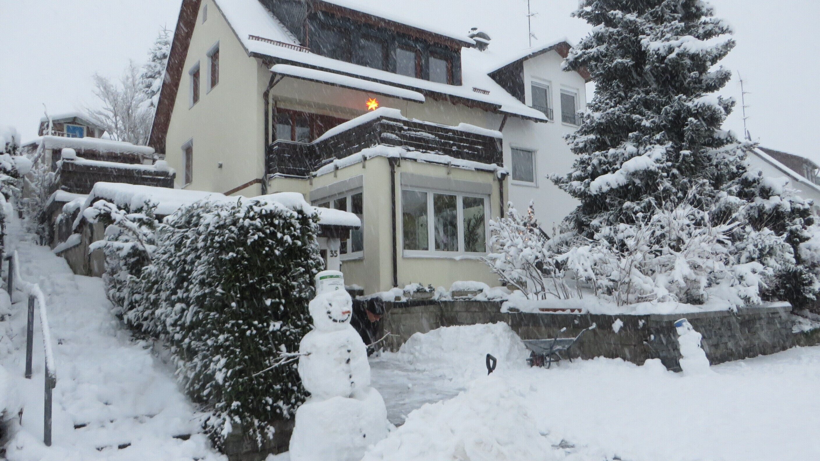 A two-story house with a snow-covered roof and a visible chimney.