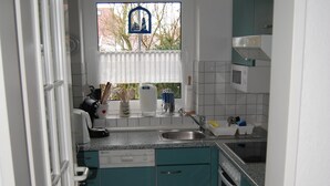 Eine kompakte Küche mit türkisfarbenen Schränken, einer weißen Arbeitsplatte und einem Fenster mit Blick auf Bäume.