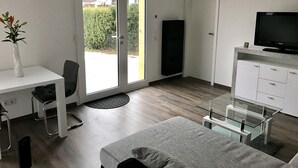 A modern hotel room with a bed, a desk with a chair, a television, and a wardrobe.