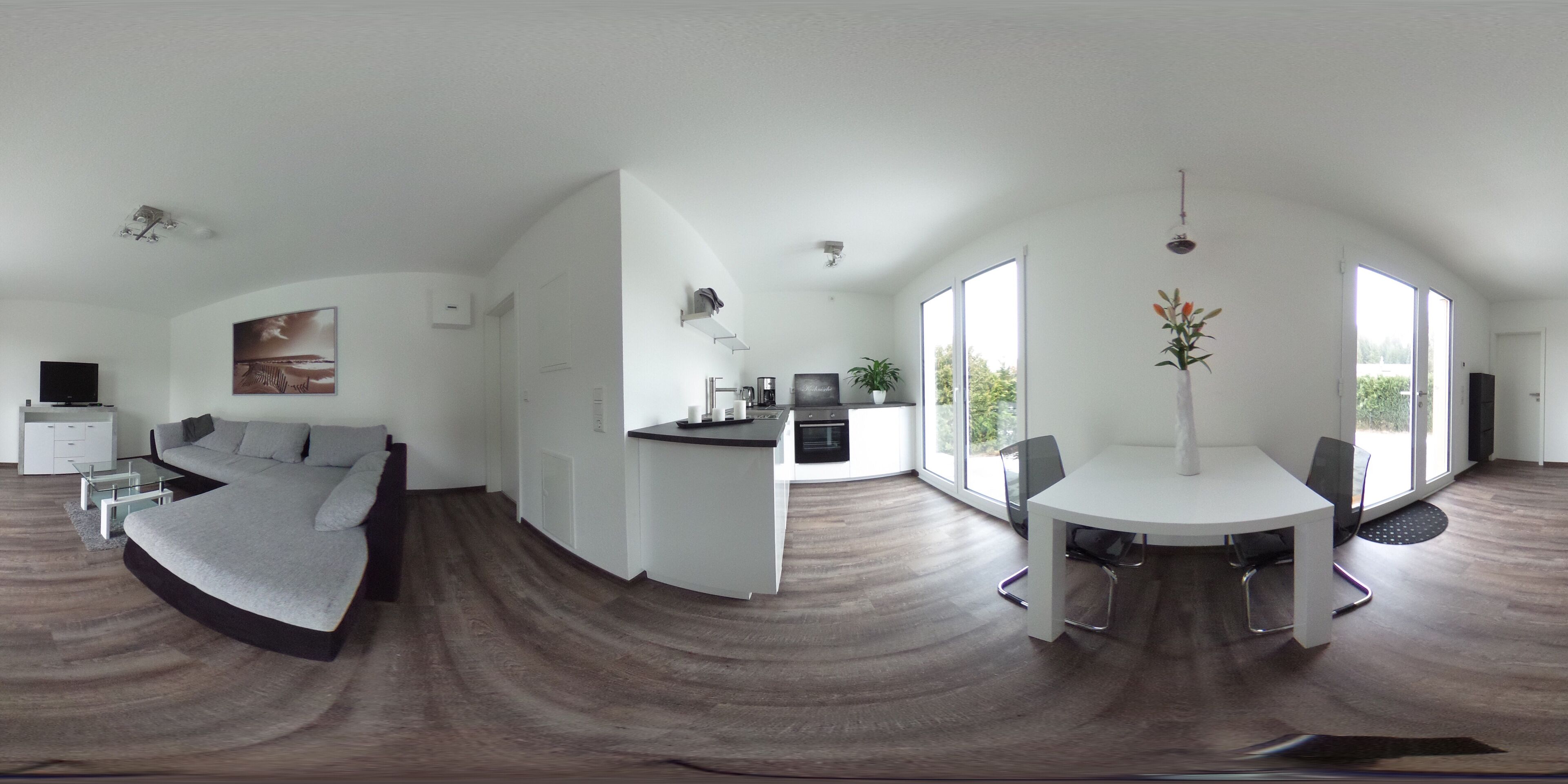 Un espace de vie moderne comprenant un canapé incurvé, un coin repas avec une table et des chaises blanches, et un espace cuisine avec une cuisinière et un évier.