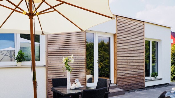 An outdoor patio with a table and chairs, a grill, and a potted plant.