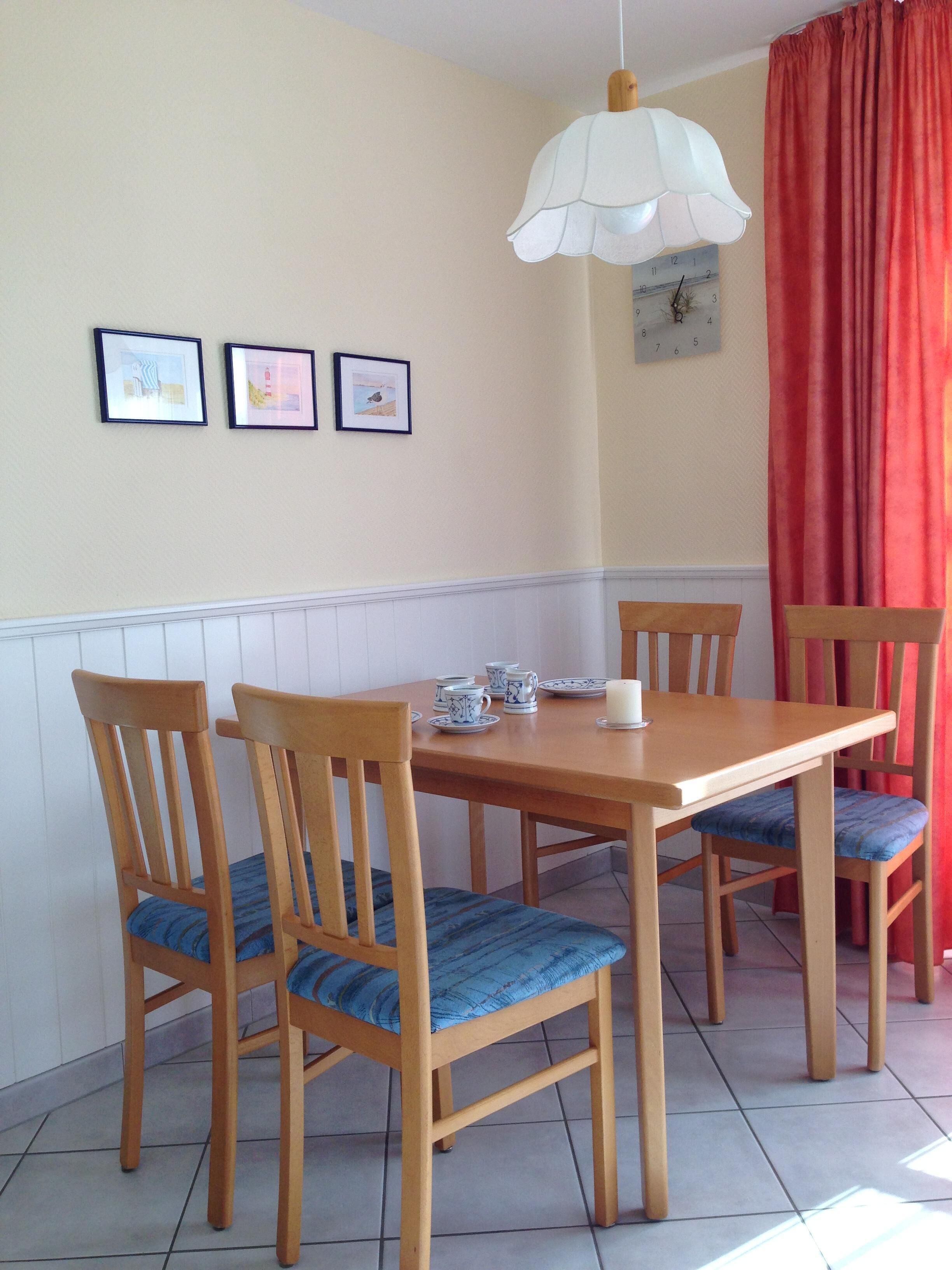 Un comedor con una mesa y sillas de madera, una lámpara colgante blanca y un reloj de pared.