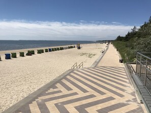 A beach with a paved walkway leading to the sea, lined with beach chairs and a lifeguard tower. - Dream vacation Wyk Südstrand - WLAN - comfortable vacation apartment with terrace (Schleswig Holstein)