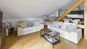Un salon de style industriel, avec un canapé blanc, une table basse en bois et une cuisine en arrière-plan.