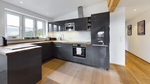 Une cuisine moderne avec des meubles de couleur sombre, un îlot central et une vue dégagée grâce à de grandes fenêtres.