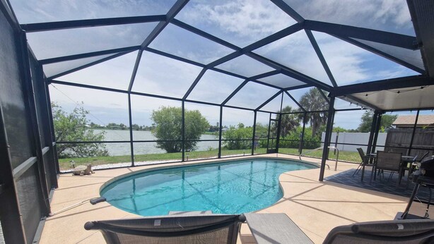 A covered outdoor swimming pool with two lounge chairs and a barbecue area. - House with solar heated pool and lake view! (Port Charlotte)