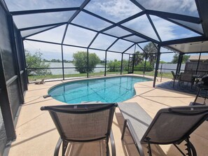 A covered outdoor swimming pool with two lounge chairs and a barbecue area. - House with solar heated pool and lake view! (Port Charlotte)