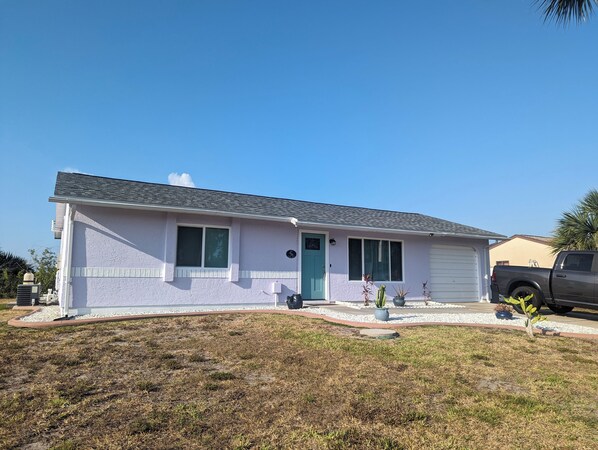 A single-story house with a light-colored exterior, a green door, and a garage. - House with solar heated pool and lake view! (Port Charlotte)
