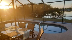 A poolside area with a table and chairs, surrounded by a glass enclosure, and a view of a lake. - House with solar heated pool and lake view! (Port Charlotte)