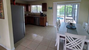 A kitchen with a refrigerator, sink, and cabinets, a dining area with a table and chairs, and a sliding glass door leading to an outdoor area. - House with solar heated pool and lake view! (Port Charlotte)