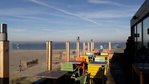 An outdoor seating area with wooden tables and chairs, overlooking a beach. - Holiday house near the beach, child-friendly, high quality, Weber grill, WiFi free (Dornum)
