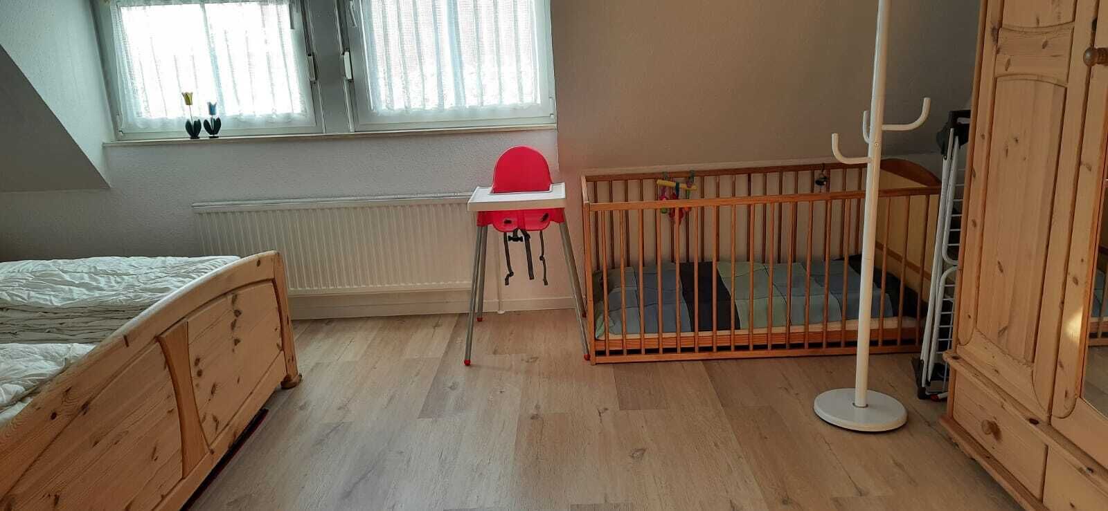 A room with a wooden bed, a crib with a red seat, a radiator, and a window with curtains.