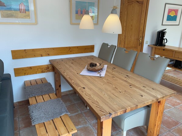 A wooden dining table with benches, a coffee maker, and framed artwork on the wall.