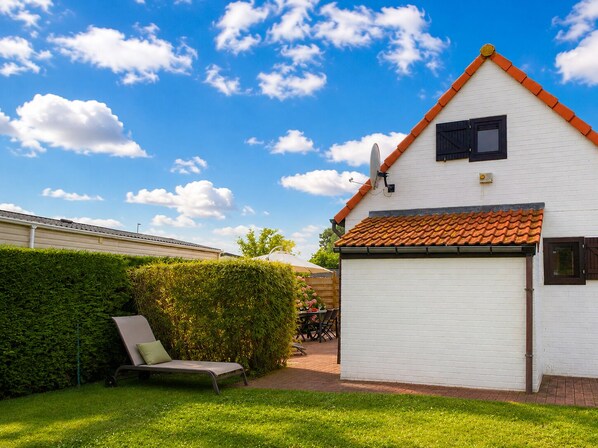 A white house with a red-tiled roof, a garage, and a lawn with a lounge chair.