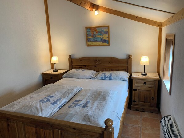 Een slaapkamer met een houten bed, twee nachtkastjes met lampen, een bijzettafeltje, een houten hoofdbord, een schilderij aan de muur en een raam met uitzicht.