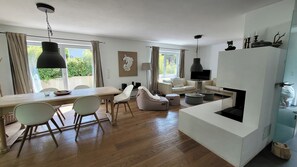 A modern living room with a dining area, a fireplace, and a large window with curtains.