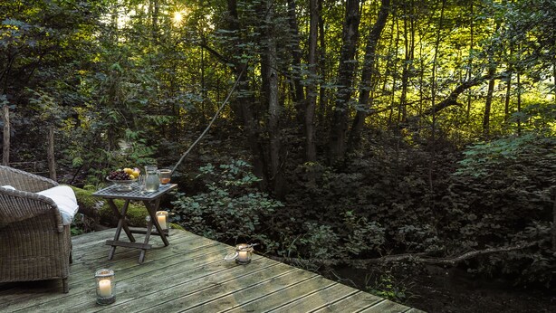 A wooden deck with wicker furniture and candles, surrounded by dense forest. - Tegernsee Chalet vacation homeexceptional (Gmund am Tegernsee)
