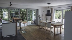 A modern kitchen with a wooden island, a dining area with a table and chairs, and large sliding glass doors leading to a garden. - Tegernsee Chalet vacation homeexceptional (Gmund am Tegernsee)