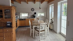 A kitchen with wooden cabinets, a dining table with chairs, and a clock on the wall. - Anti-allergy and comfortable vacation home (Dornum)