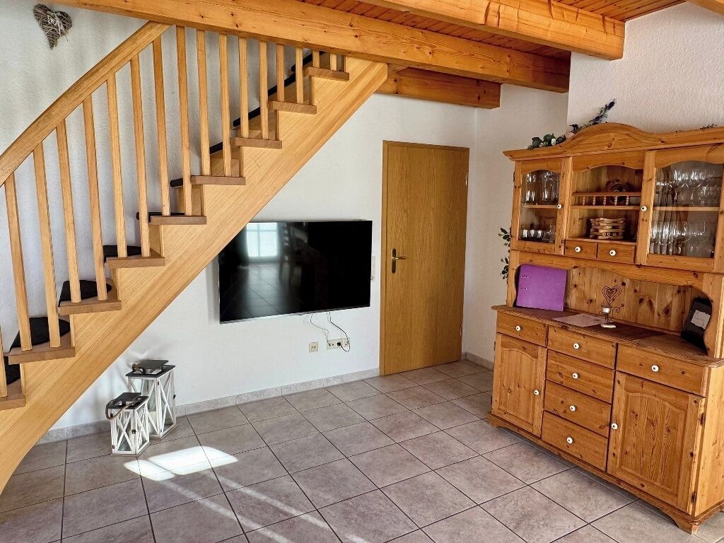 Un escalier en bois, un téléviseur à écran plat, un meuble contenant de la verrerie et une porte.