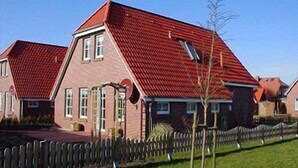 A residential building with a red roof, brick walls, and a wooden fence. - Anti-allergy and comfortable vacation home (Dornum)