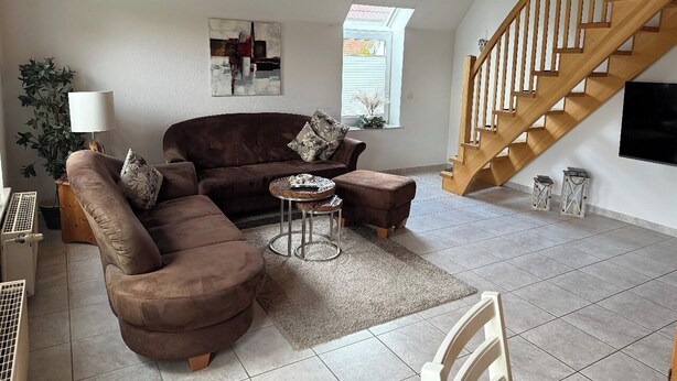 A living room with a brown sofa, a round coffee table, and a wooden staircase. - Anti-allergy and comfortable vacation home (Dornum)