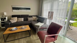 Ein modernes Wohnzimmer mit einer Eckcouch, einem Holztisch, einem roten Sessel und einem großen Fenster mit Vorhängen.