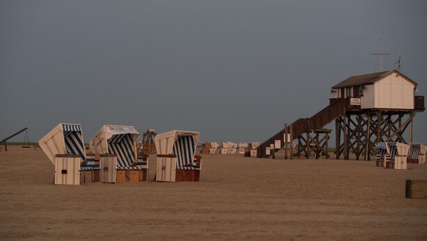 Ein Strand mit mehreren gestreiften Liegestühlen und einer Holzkonstruktion mit einer Treppe.