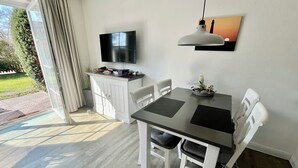 Ein moderner Essbereich mit Tisch, Stühlen, einem Fernseher und einer Pendelleuchte.