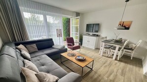 Ein modernes Wohnzimmer mit einer Eckcouch, einem Esstisch mit Stühlen, einem Fernseher und einem Schrank.