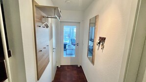 Ein Flur mit einer Holztür, einem Spiegel und Blick in einen Raum mit Bett und Fenster.
