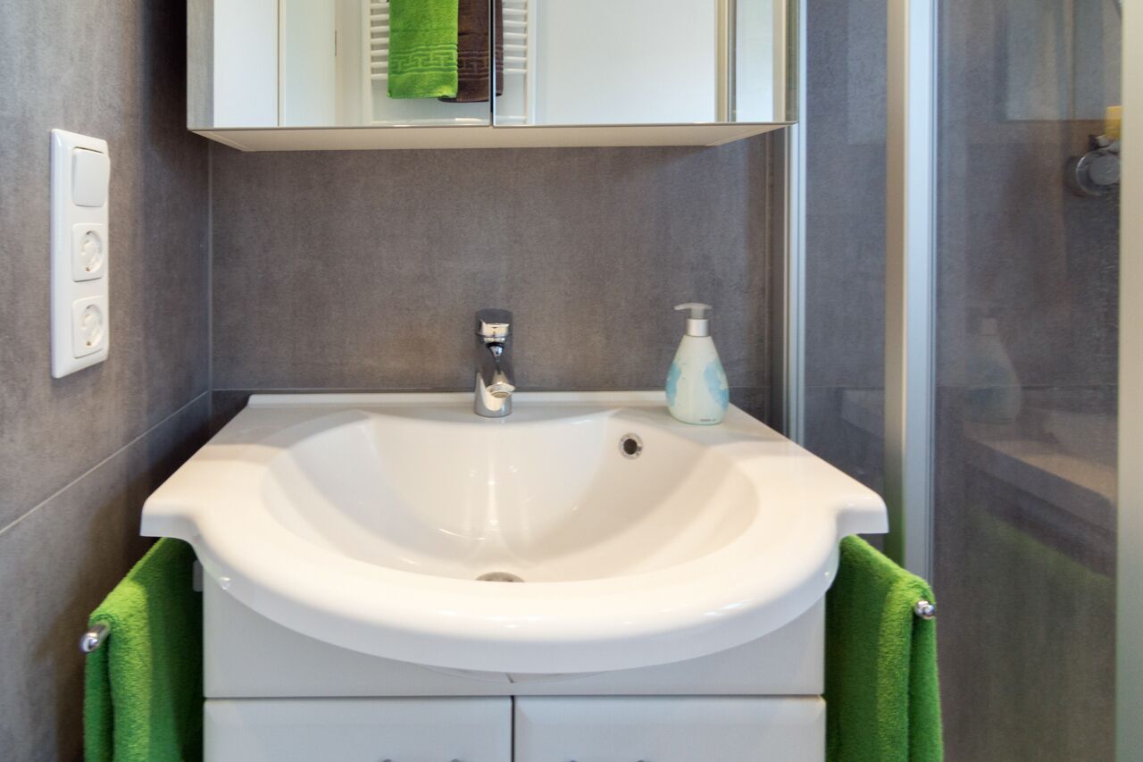 A bathroom with a white sink, green towels, a mirror, and a shower area.