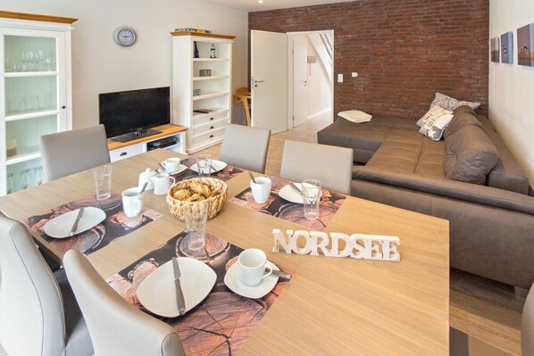 Un salon moderne avec un coin repas, comprenant une table en bois dressée pour quatre personnes, un canapé et un téléviseur.