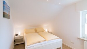 Een slaapkamer met een bed, nachtkastjes, een raam en een wandlamp.
