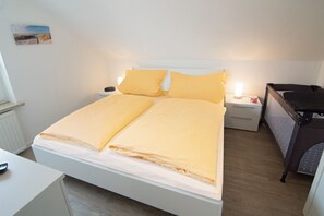 A neatly made bed with yellow bedding, a bedside table with a lamp, and a small nightstand. - Vacation apartment Norddeich (Norddeich)