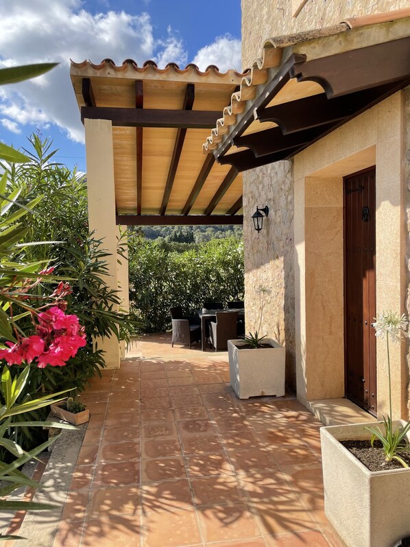 A covered patio with a tiled floor, a wooden pergola, and a stone wall.