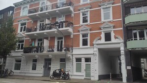 Un edificio de varios pisos con un estilo arquitectónico clásico, con balcones con barandillas y plantas en macetas.